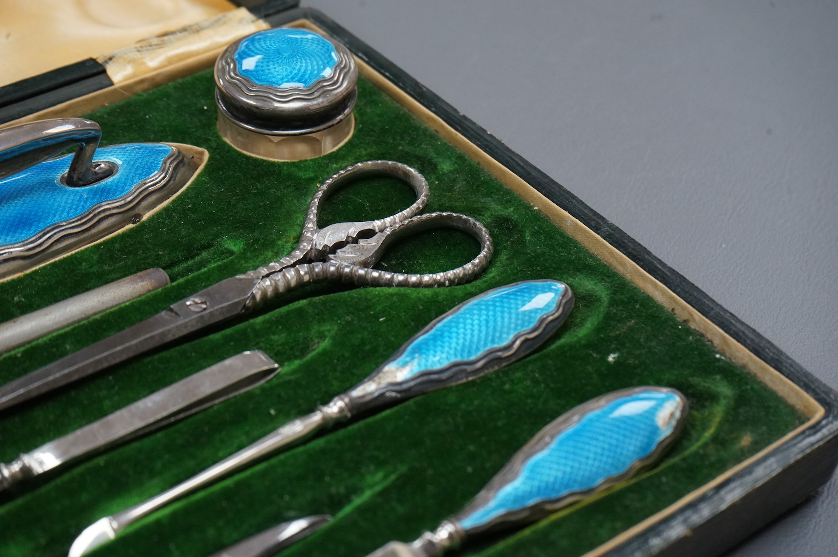 A cased George V eight piece (ex 9 piece) manicure and toilet jar set, comprising seven silver and enamel mounted items, Boots Pure Drug Company, Chester and Birmingham, 1910, together with a matching pair of steel sciss